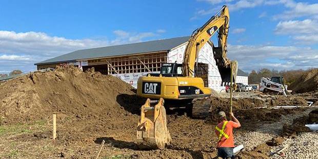 Worker standing in a trench with excavator digging in the background. trench.